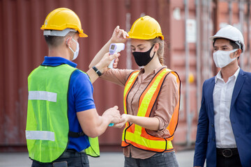 manager wear face mask scanning body temperature and using hand sanitizer alcohol gel to worker before entering working over Containers box at logistic Cargo during Coronavirus or Covid 19 pandemic