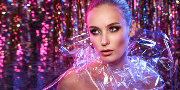 High Fashion model girl in colorful bright neon lights posing in studio through transparent film. Portrait of beautiful woman in UV. Art design colorful make up. On colourful vivid background