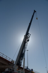 Crane almost silhouetted by sun on a highway  bridge construction site. Dramatic, diagonal, vertical. Copy space. 
