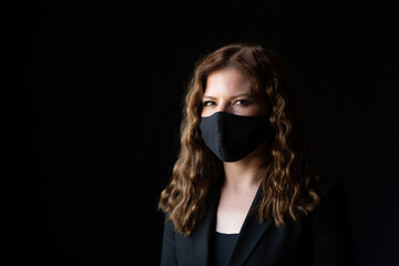 Young curly woman wearing a protective black face mask during the Coronavirus pandemic. Portrait on a black background.