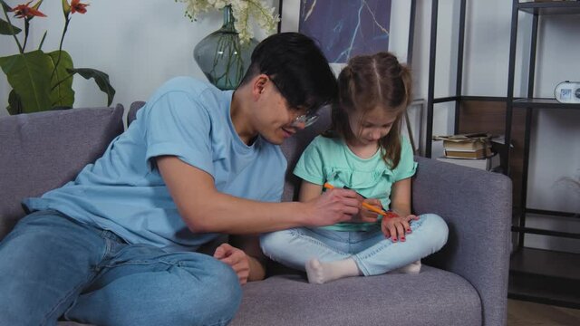 Asian young father playing with little caucasian daughter. Kid and dad drawing picture on hands at home. Happy family, recreational pursuit. . 4k slow motion