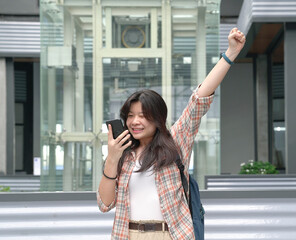 Beautiful Asian woman react with joy by raising her had in jubilation while looking at her cellphone. Inside building setting.