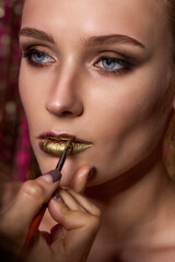 Young beautiful girl applying make-up gold lips by make-up artist close up