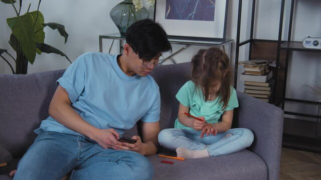 Asian father and caucasian daughter drawing pictures on hands. Happy family leisure with child girl. Cute kid having fun with parent. Dad and preschool daughter enjoy activity.