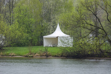 Summer cozy gazebo made of durable white tarpaulin on the shoreline by the lake for tourists