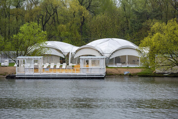 Summer cozy gazebo made of durable white tarpaulin on the shoreline by the lake for tourists