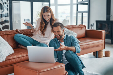 Beautiful young couple using laptop and smiling while spending time at home