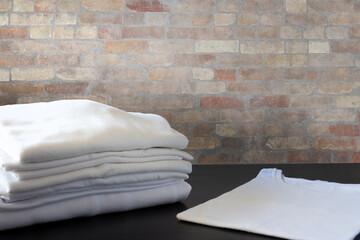Pile of white clothes in front of brick wall and on black floor. Shirt and tshirts