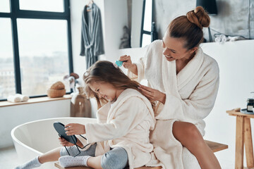 Beautiful young mother combining her daughter hair while doing morning routine