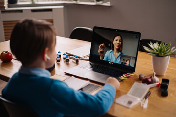 A Preteen boy uses a laptop to make a video call with his teacher. The Screen shows an online lecture with a teacher explaining the subject from class. E-Education Distance Learning, Homeschooling.