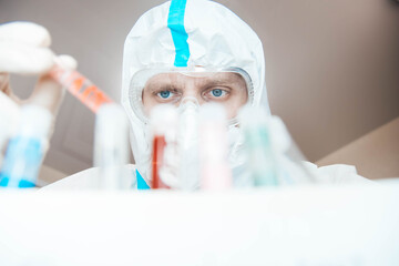 male scientist biologist examines test tubes in the laboratory in an epidemiological suit