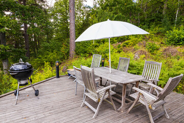 View of wooden patio of typical  wooden Swedish house with table, barbecue, chairs and sitting area with umbrella.  Sweden. Europe.