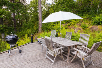 Obraz premium View of wooden patio of typical wooden Swedish house with table, barbecue, chairs and sitting area with umbrella. Sweden. Europe.
