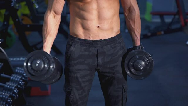 Shirtless muscular man training biceps with dumbbells. Naked torso of a bodybuilder doing functional training with heavy weights. Sport fitness healthy lifestyle concept.