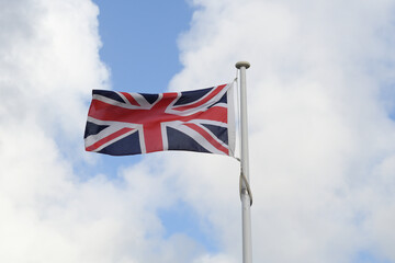 The Union Jack, or Union Flag, flying on a windy day, with bright blue sky and white clouds in the background