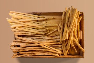 Italian breadsticks with sesame seeds and with olives in wooden tray on beige background in top view
