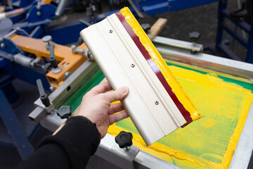 Squeegee for Serigraphy silk screen print process in hand at clothes factory. Frame, squeegee and...