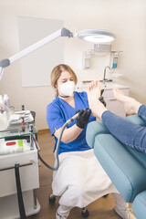 Young Chiropodist / Podiatrist with patient in cosmetic  treatment. Podiatry drill. Professional foot care. Medical mask (FFP2)