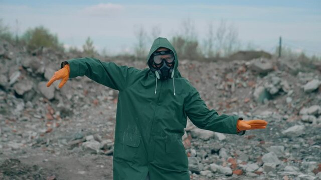 Man in safety suit and respirator on garbage background. Mad man in protective costume and gas mask dancing in abandoned place in radioactive zone.