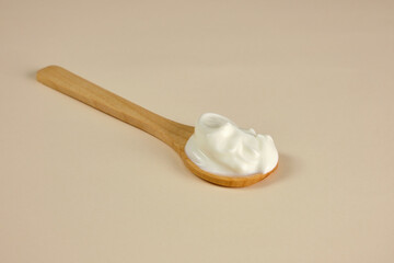 Wooden spoon with mayonnaise, yogurt, sauce on a cream, light brown background