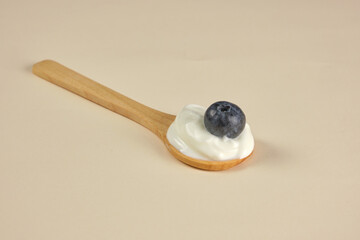 Wooden spoon with mayonnaise, yogurt and a blueberry with a cream colored background, light brown