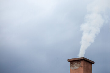 Selective blur on a smoking chimney rejecting white fume brick on the roof of an individual residential house exhausting little fumes at dusk, during a cloudy afternoon...