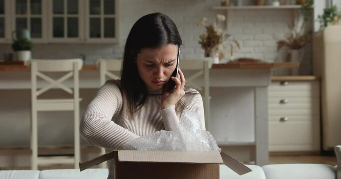 Dissatisfied young woman sit on sofa open parcel box looks inside check purchased delivered damaged items feels upset. Client of postal delivery services calls to customer support express complaints