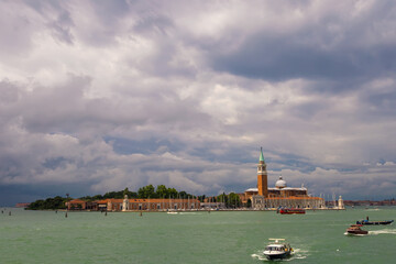 Basilica of San Giorgio Maggiore at sunset. Boats are sailing along the canal. Summer evening, dark clouds in the sky. Italy, Venice.