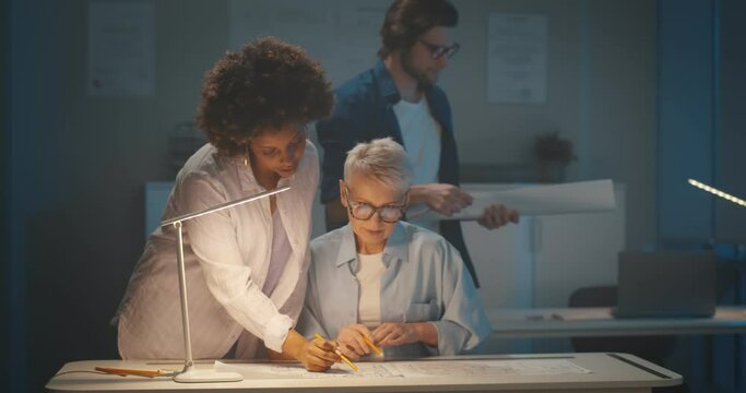 Team of multiethnic architects working on construction plans late in dark office