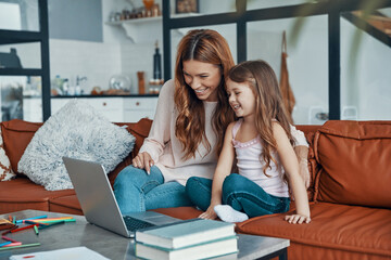 Mother and her daughter bonding together and smiling while using laptop at home