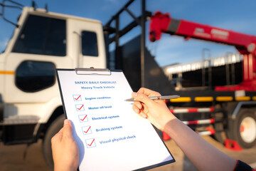 Action of mechanic worker is using the daily checklist form to verify and inspection a heavy truck vehicle (blurred background). Industrial safety working concept photo. Close-up and selective focus.