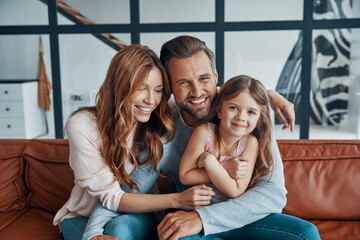 Happy young family smiling and looking at camera while bonding together at home