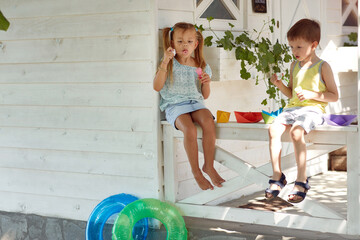 boy and girl sitting on a porch playing with paper boats, making soap bubbles - Powered by Adobe