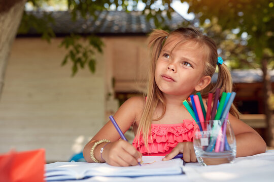 cute little girl thinking, looking up, while drawing with felt tip pen
