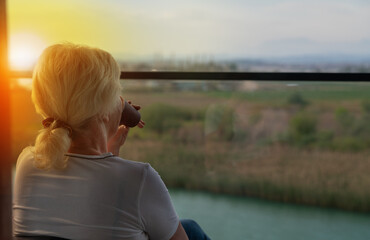 Woman sipping coffee on a balcony at sunrise overlooking a river