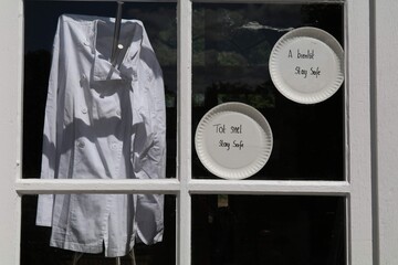 chef's jacket and signs in the window due forced closure of restaurants as safety measure to fight corona virus. The signs say in French "see you soon, stay safe" and Dutch "see you soon, stay safe"
