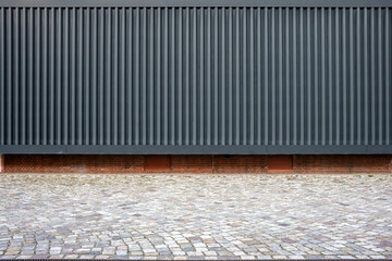black corrugated sheet metal aluminum facade and concrete wall of a warehouse and a cobblestone road as backdrop - obrazy, fototapety, plakaty