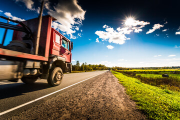Truck rides along the forest road which is in the field with haystacks lit by the sun on a blue sky background. High contrast and obscured image