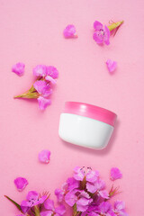 Creative beauty fashion concept photo of flowers plants petals with cosmetic recyclable bottle lotion cream on pink background.