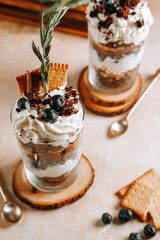 Two glasses with a layered dessert trifle with chocolate, cream, cookies and blueberries
