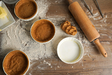 Several small baking forms with dough, flour and rolling pin on a kitchen table