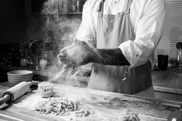 Man chef making italian noodles tagliatelle out of dough in the kitchen black and white