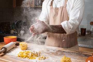 Man chef making italian noodles tagliatelle out of dough in the kitchen