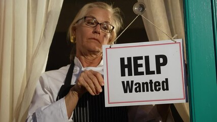 Female shop owner putting Help Wanted sign on glass door. Woman staff chef of restaurant advertising for hiring staff.