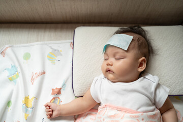 asian baby infant get fever and apply cool patch on forehead sleeping at home after vaccination. cold pad gel healing temperature. baby sick after back from hospital. - obrazy, fototapety, plakaty