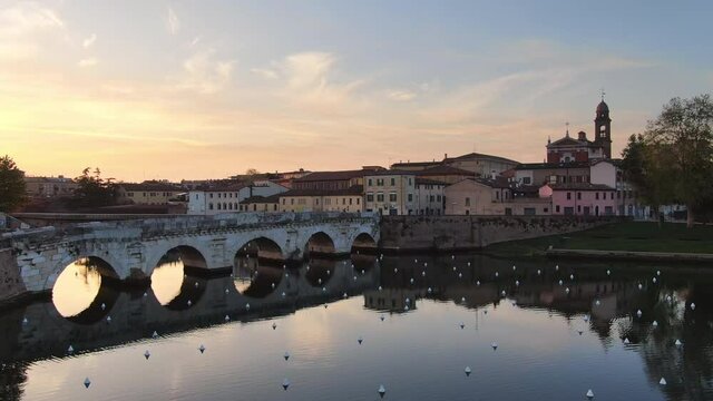 rimini city aerial view at sunrise drone rising up over tiberio bridge monument revealing historic downtown