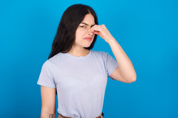 young beautiful tattooed girl wearing blue t-shirt standing against blue background smelling...