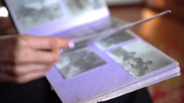 young woman with manicure looks through family album with old black and white photos of house. girl looks through her deceased relatives, family tree. concept of memory of relatives and pedigree.