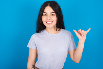 young beautiful tattooed girl wearing blue t-shirt standing against blue background showing up number six Liu with fingers gesture in sign Chinese language