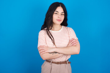 young beautiful tattooed girl wearing pink striped t-shirt standing against blue background with nice beaming smile pleased expression. Positive emotions concept